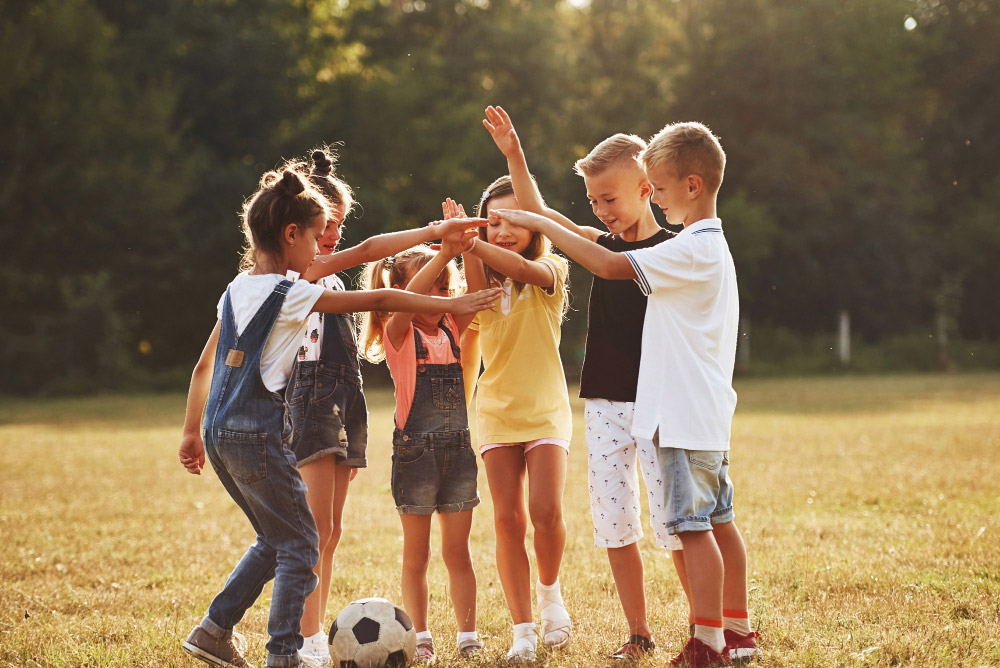 Gruppe von sechs Schulkindern stehen im Teamkreis am sonnigen Tag zusammen auf dem Feld und wollen Fußball spielen