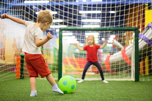 kleiner Junge schießt Ball zum Kinderfußballtor, indem ein Mädchen den Torwart spielt